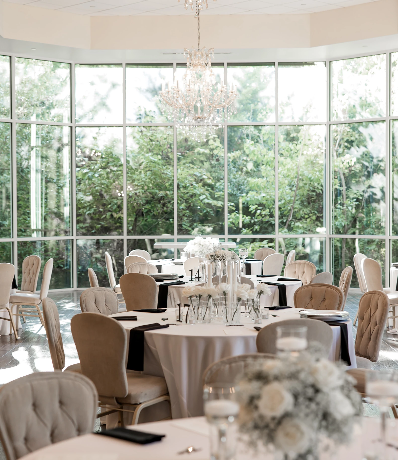 Elegant wedding reception table with white linens, pink floral centerpieces, gold-rimmed glassware, and soft gray upholstered chairs