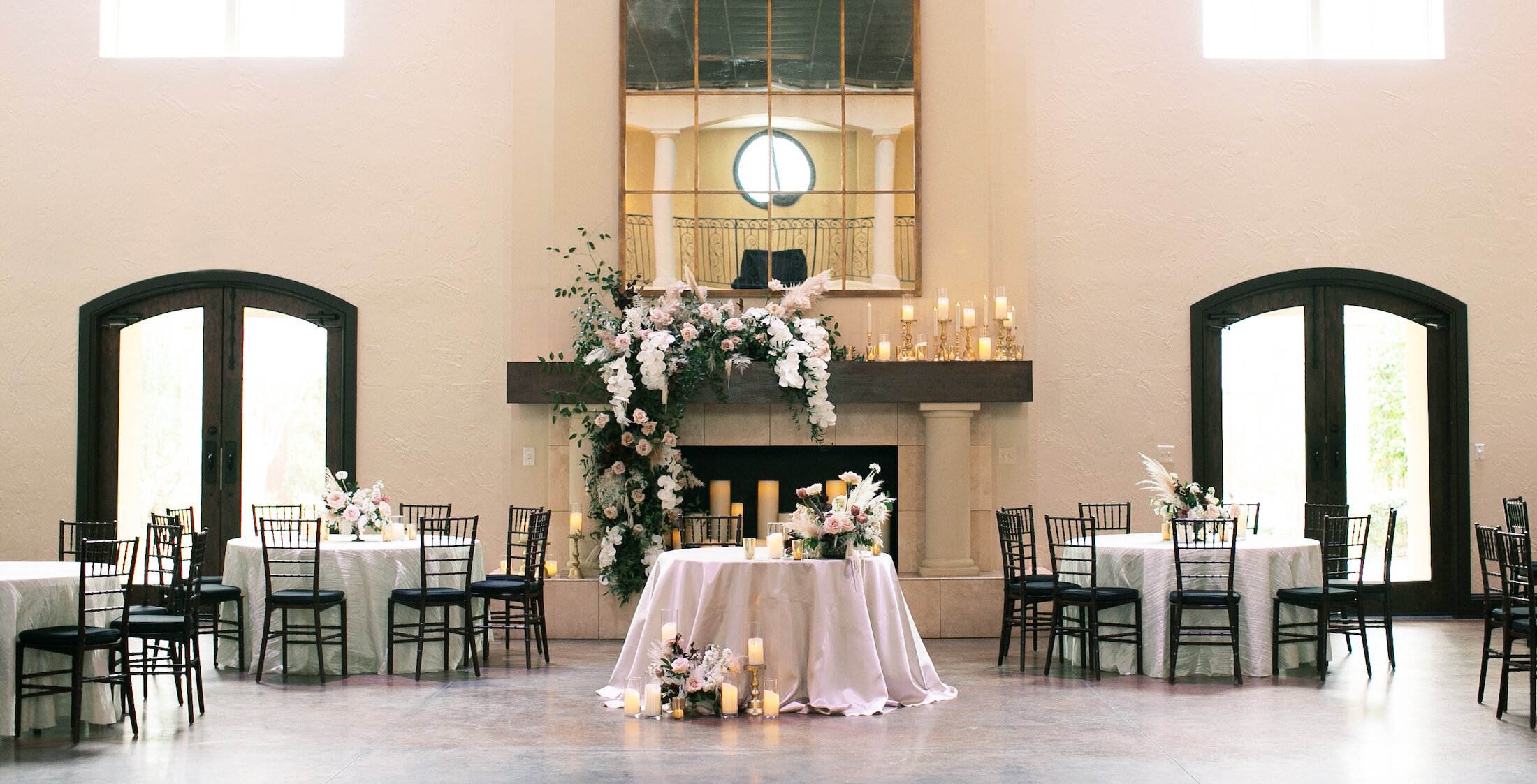 The elegant interior of a wedding reception space at Ana Villa featuring a large fireplace decorated with white and pink flowers, candles, and surrounding tables.