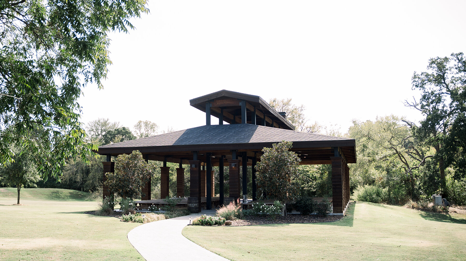 Outdoor pavilion with wooden beams and landscaped greenery on a sunny day