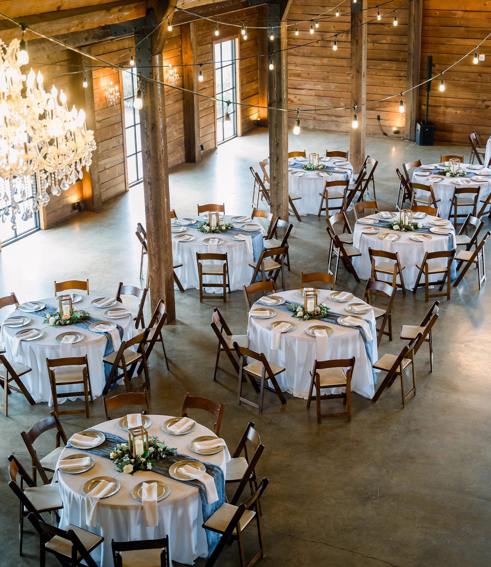 Close-up of an elegant wedding reception table with sage green linens, black chiavari chairs, white florals in bud vases, glass chargers, water goblets, and a Table 5 sign