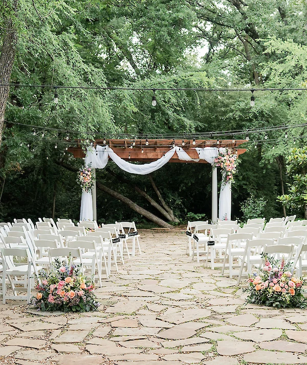 Elegant French-inspired building with cream stucco exterior, arched windows, iron balcony railing, black double doors, and lush landscaping with blooming roses.