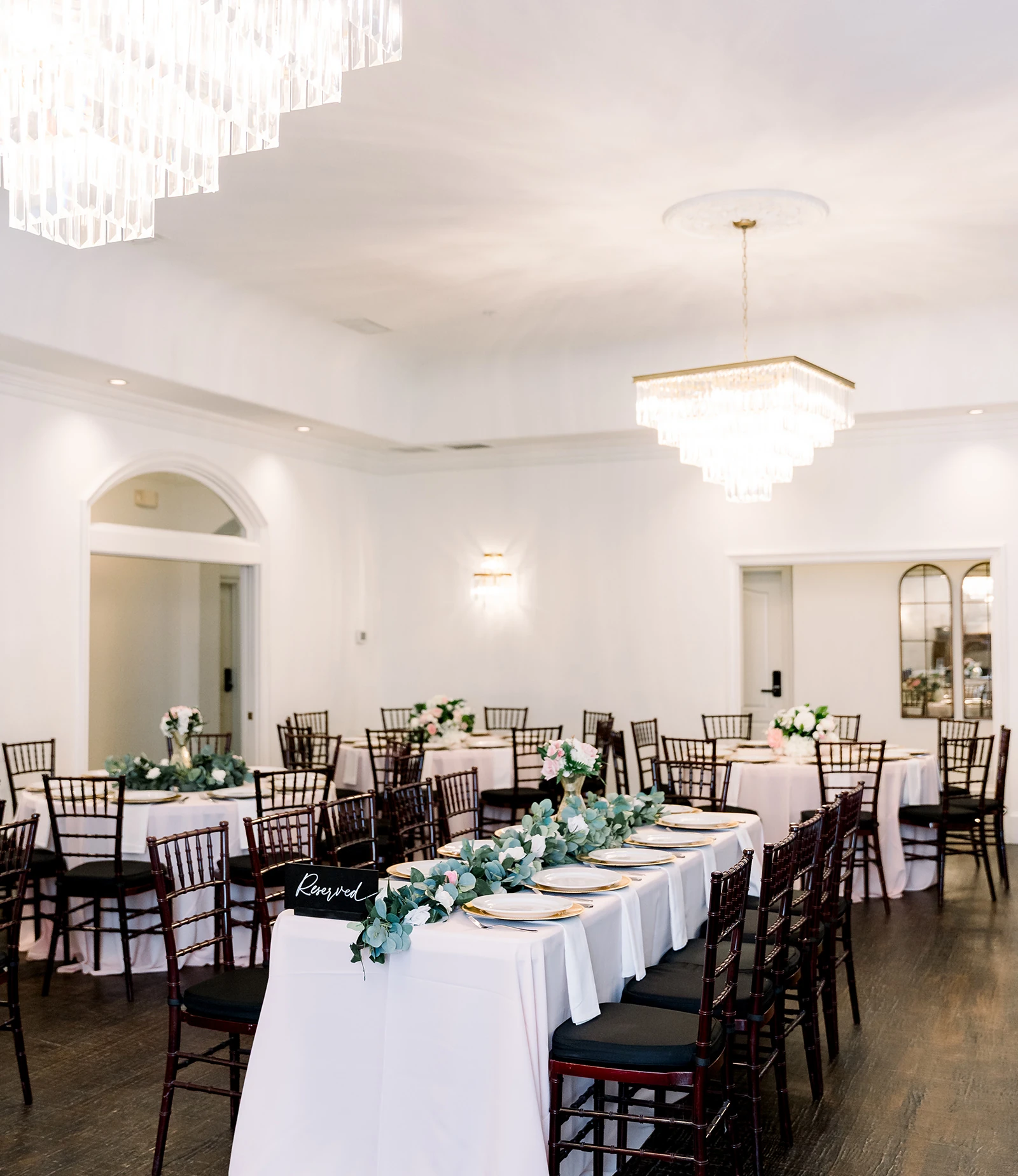Outdoor wedding ceremony setup with rows of white folding chairs on a flagstone patio, blue and white floral arrangement in the aisle, and wooden pergola overhead.