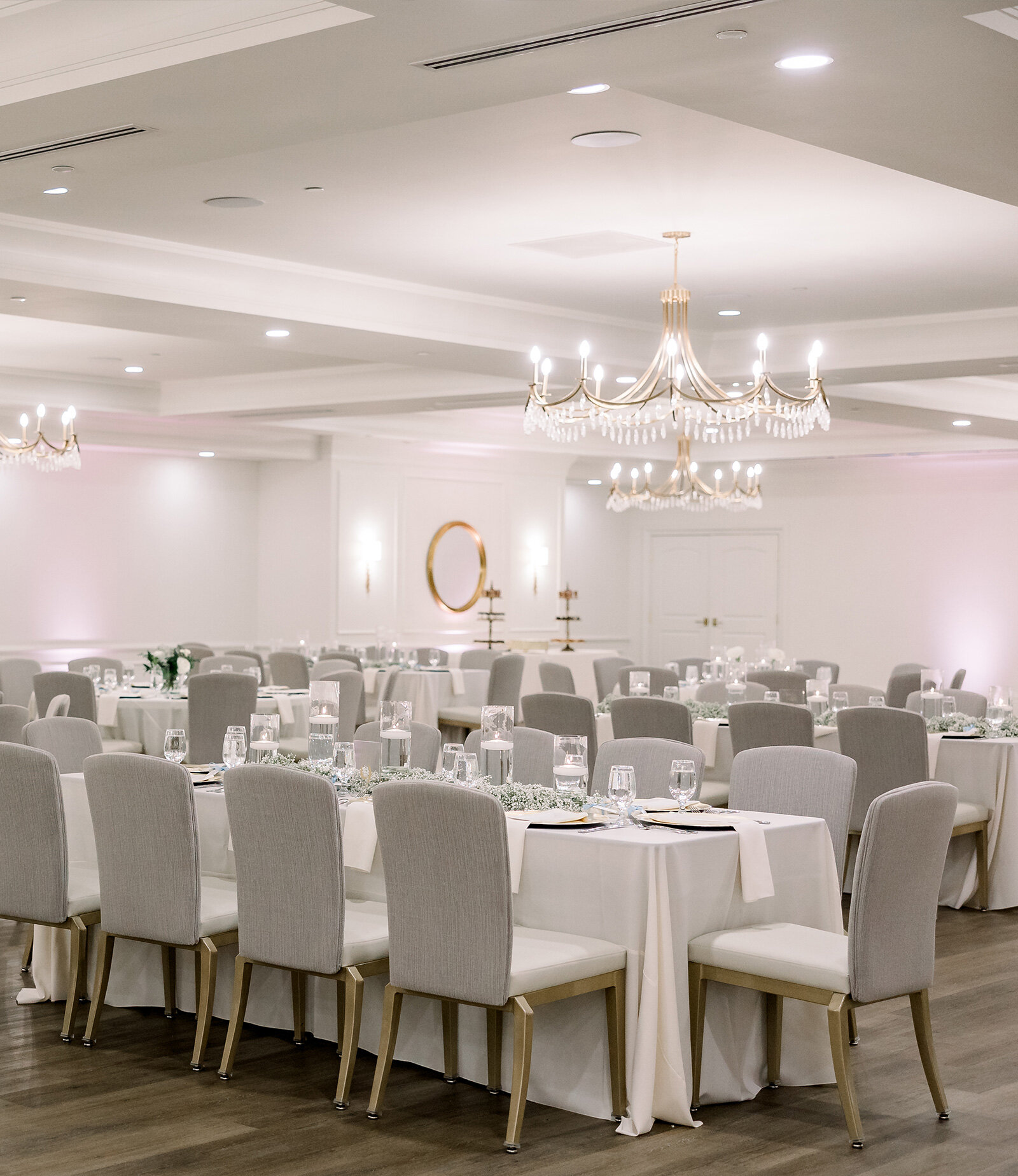 Elegant reception table with tall floral centerpieces of white and blush flowers in clear vases, surrounded by gold candlesticks with lit taper candles