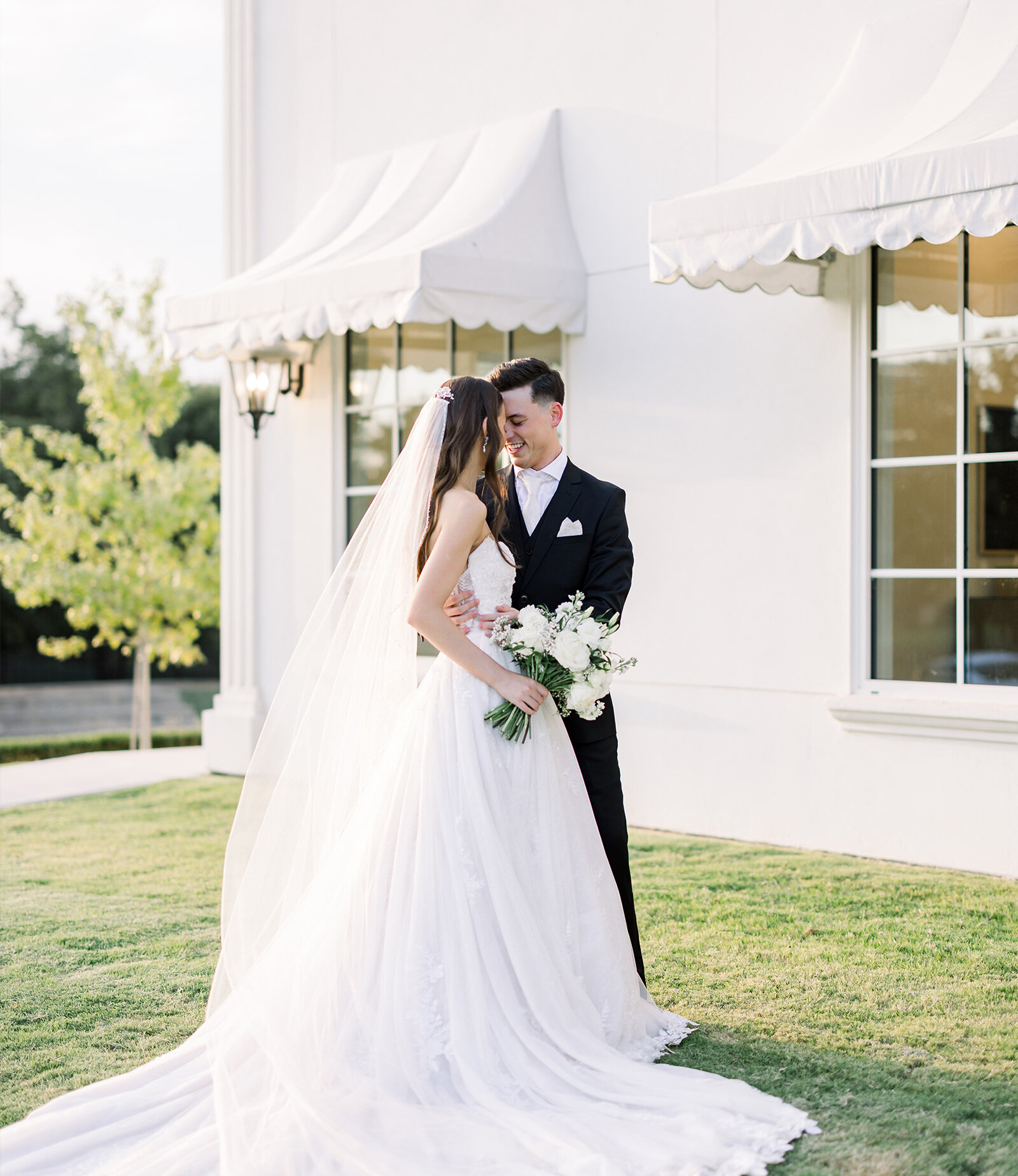 Elegant wedding reception ballroom with white linens, gray upholstered chairs, crystal chandeliers, and minimalist greenery table runners