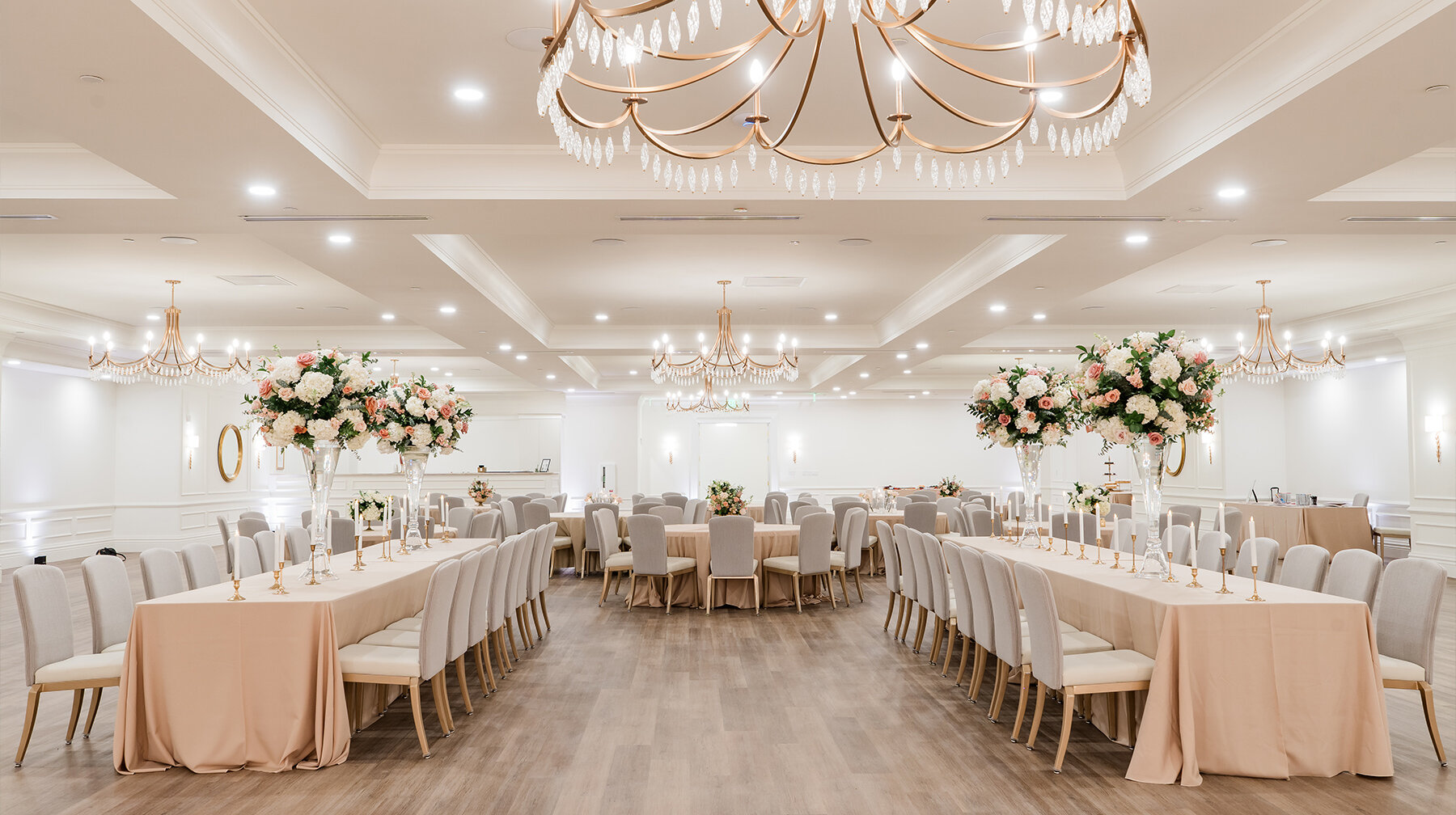Lush peach and pink floral centerpieces in tall glass vases decorating an elegant wedding reception table.