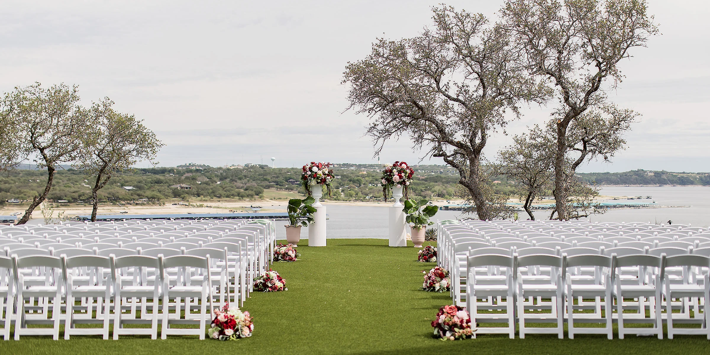 Outdoor ceremony setting overlooking Lake Travis, with a large floral arch at the front of the aisle
