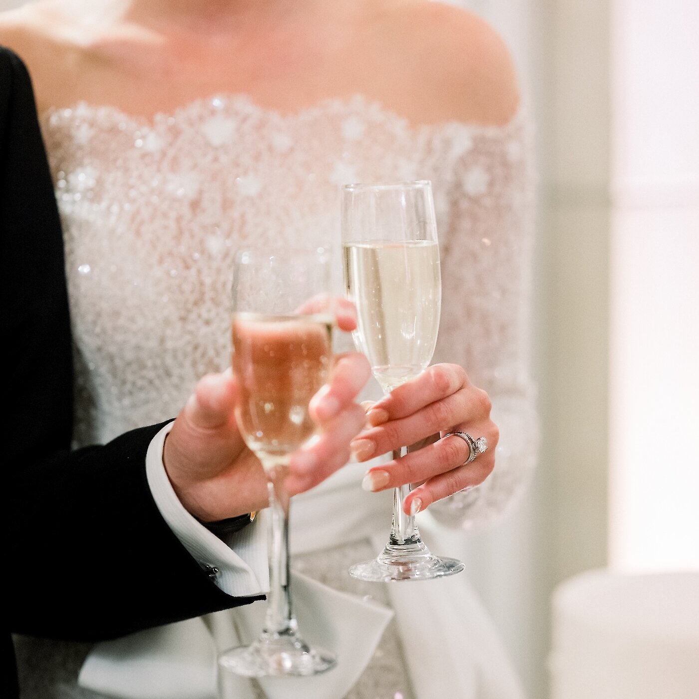 The bride, wearing a sparkling off-the-shoulder gown, and the groom hold flutes of champagne for a wedding toast.