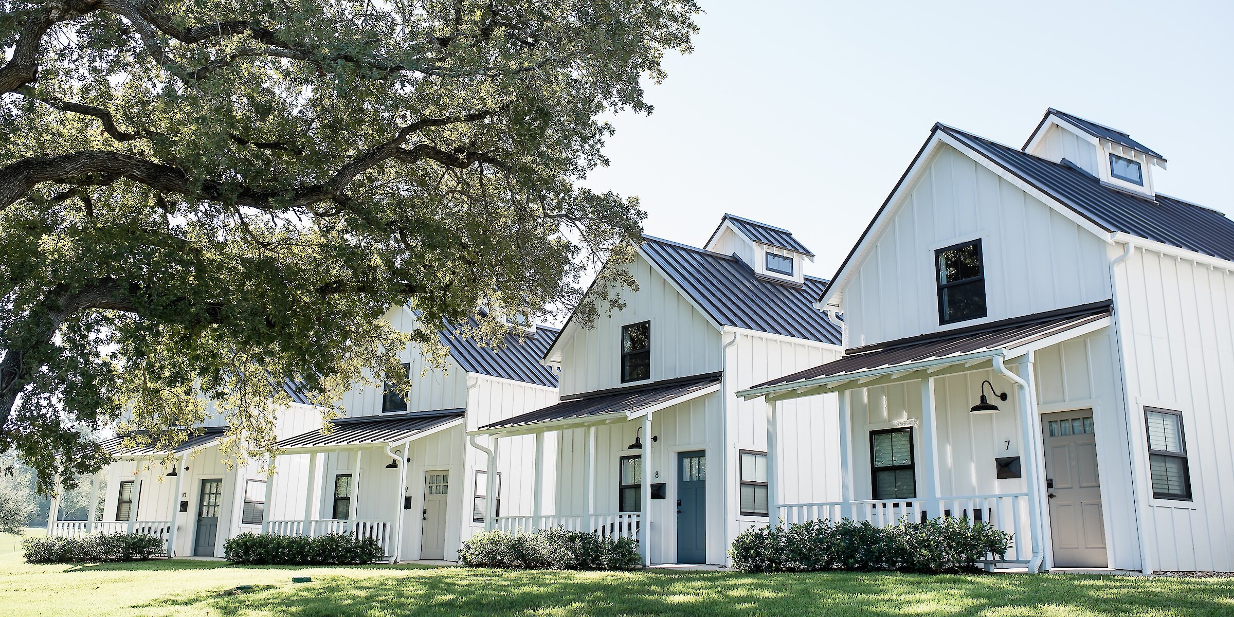 A row of white modern farmhouse-style cottages with dark metal roofs and front porches at The Lakota.