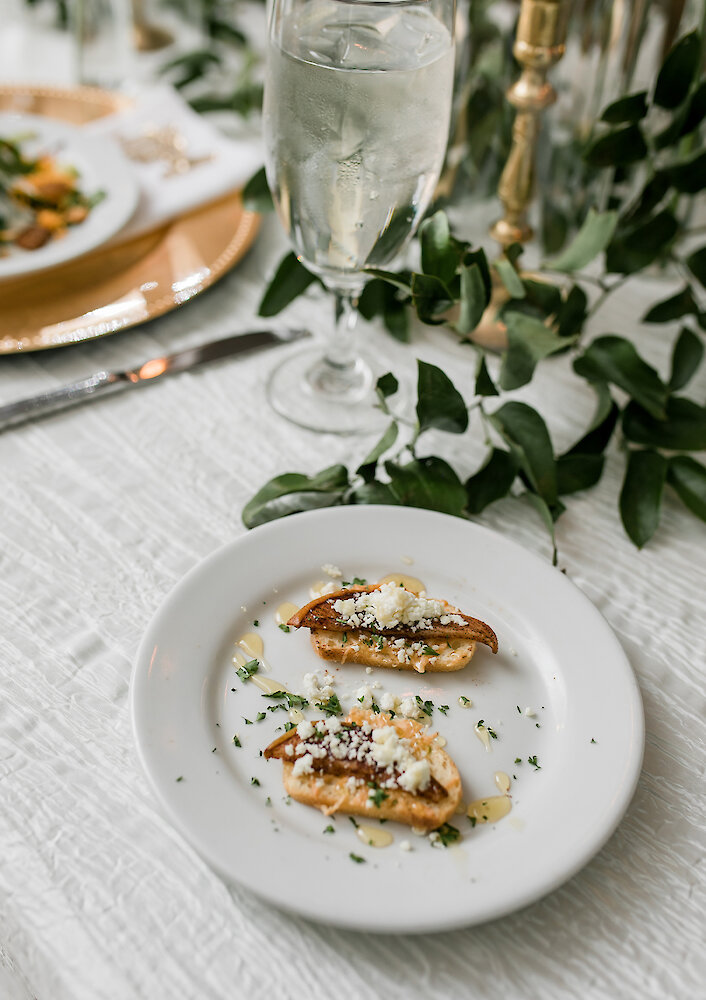 An elegant plated dinner featuring beef, chicken, rice pilaf, grilled asparagus, and a dinner roll on a gold charger plate.