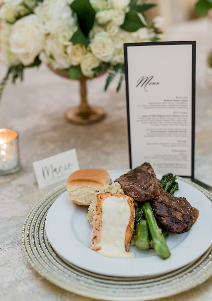 A plated dinner salad with a dinner roll and butter, served on a white plate atop a gold charger plate at a wedding reception.