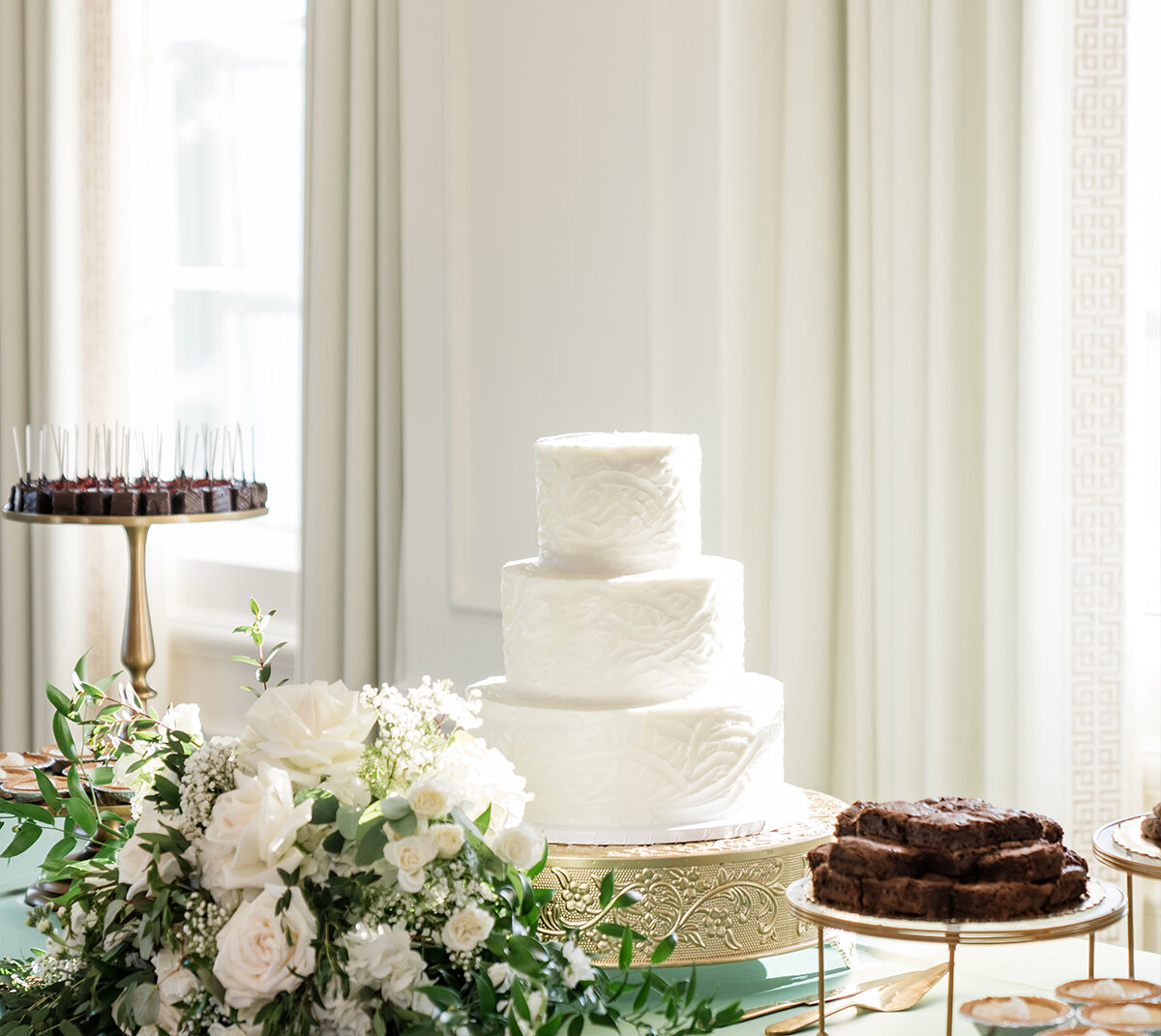 An overhead flat lay of two slices of wedding cake on white plates with forks, styled with white flowers on a blue and white toile tablecloth.