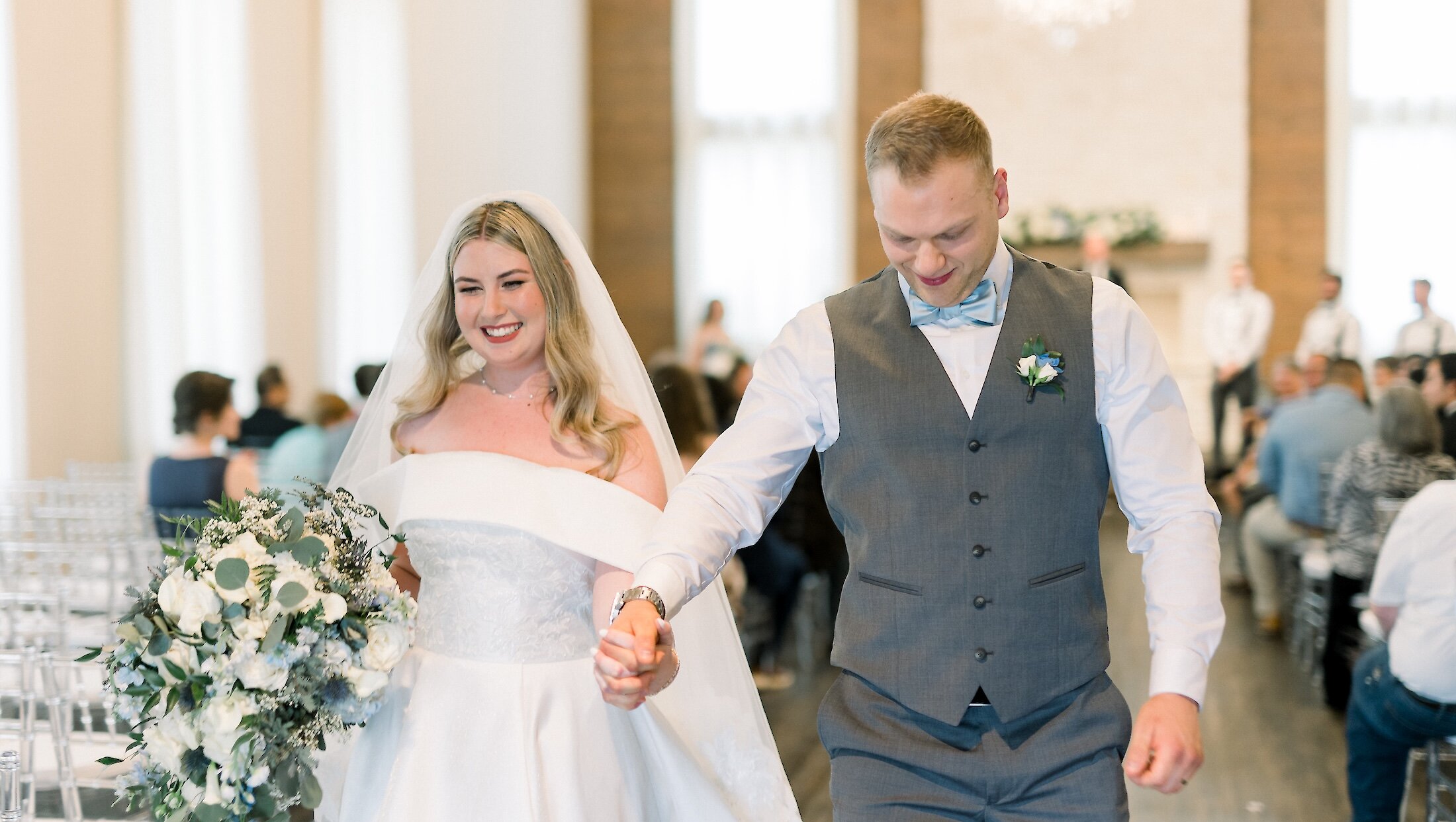 A happy bride and groom holding hands as they smile and walk down the aisle after their marriage ceremony.