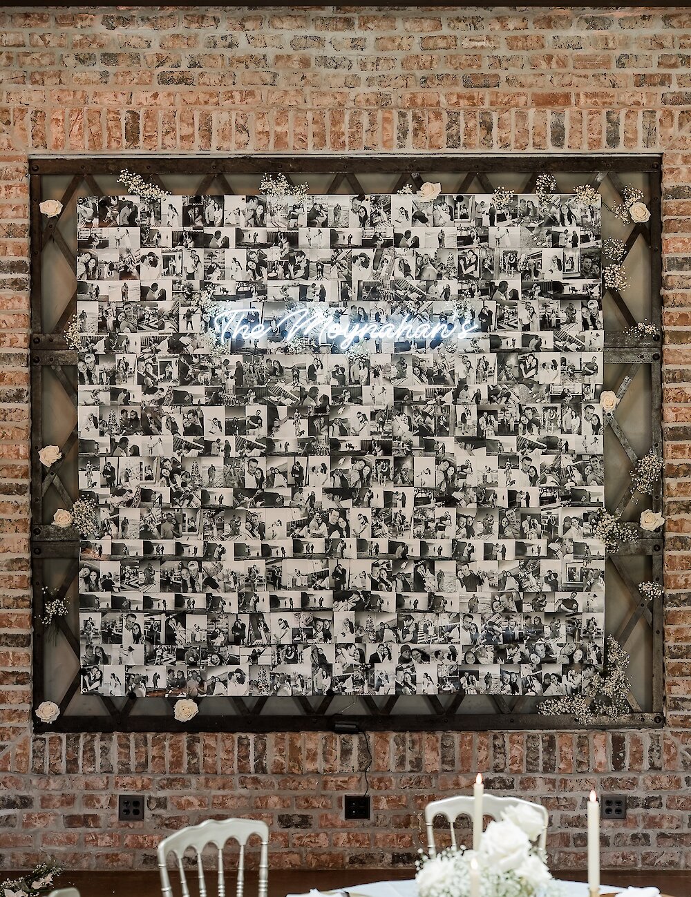 A wedding reception photo wall featuring hundreds of black and white pictures and a glowing neon sign that reads 'The Moynihans' on a brick background.