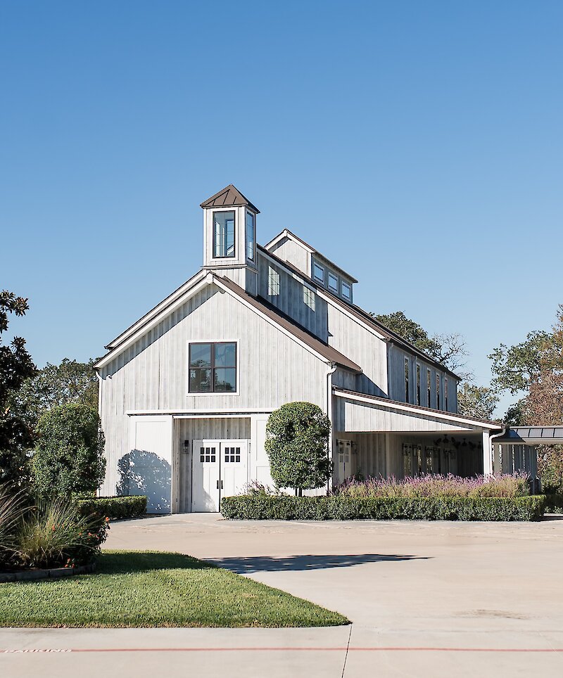 The exterior view of the white, weathered wood barn at the Arrowhead Hill wedding venue under a clear blue sky.