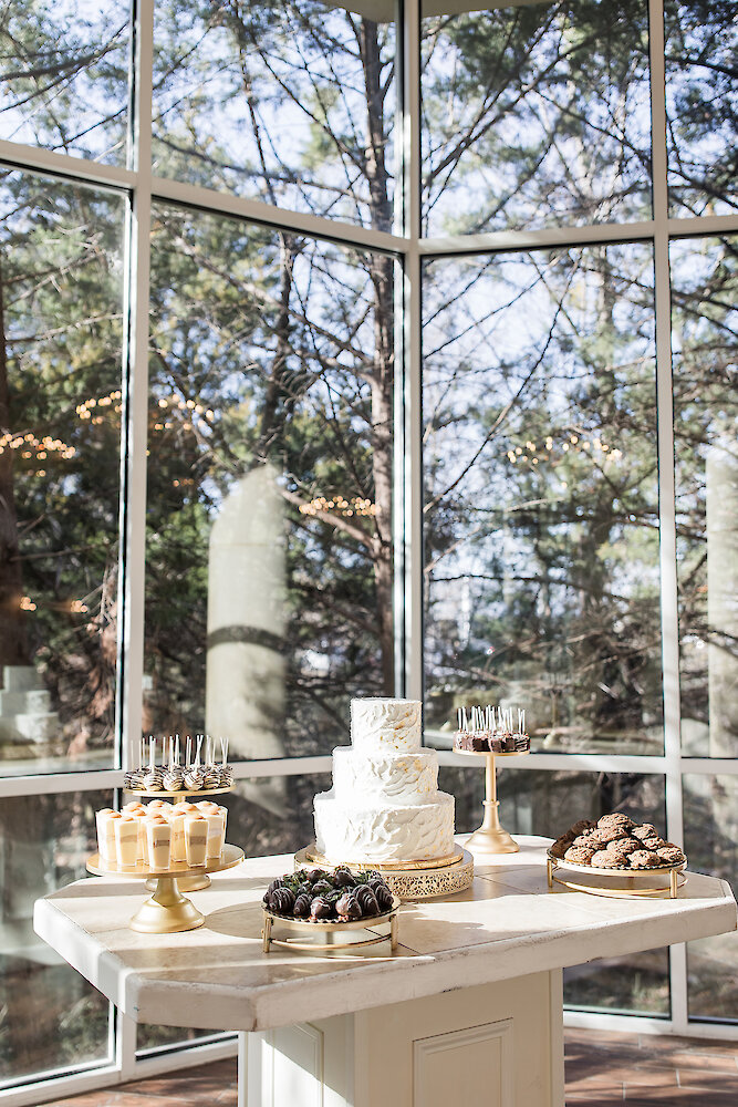 Wedding dessert display featuring a white textured tiered cake surrounded by cake pops, cookies, and chocolate-covered strawberries.