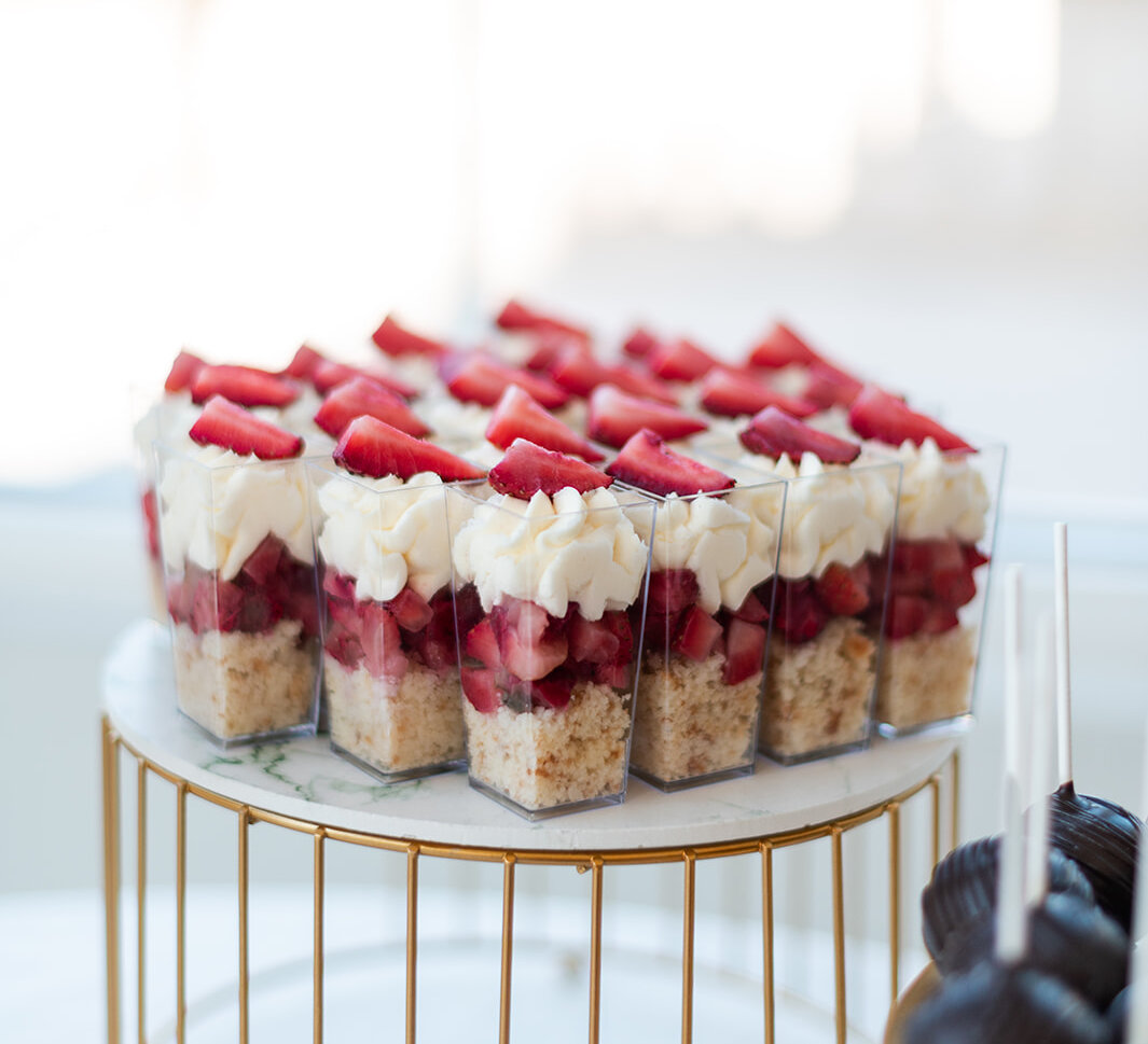 Strawberry shortcake dessert shooters arranged on a gold wire stand at a wedding dessert table.