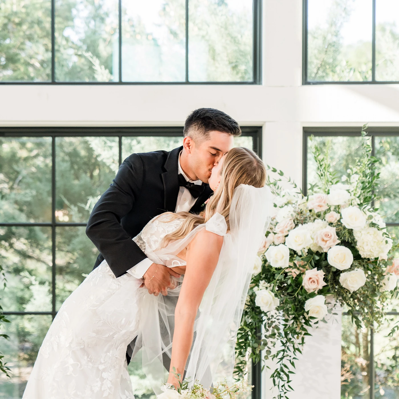 A wedding guest book table featuring a gold framed sign, two blue Instax cameras, and a small floral arrangement with pink roses.