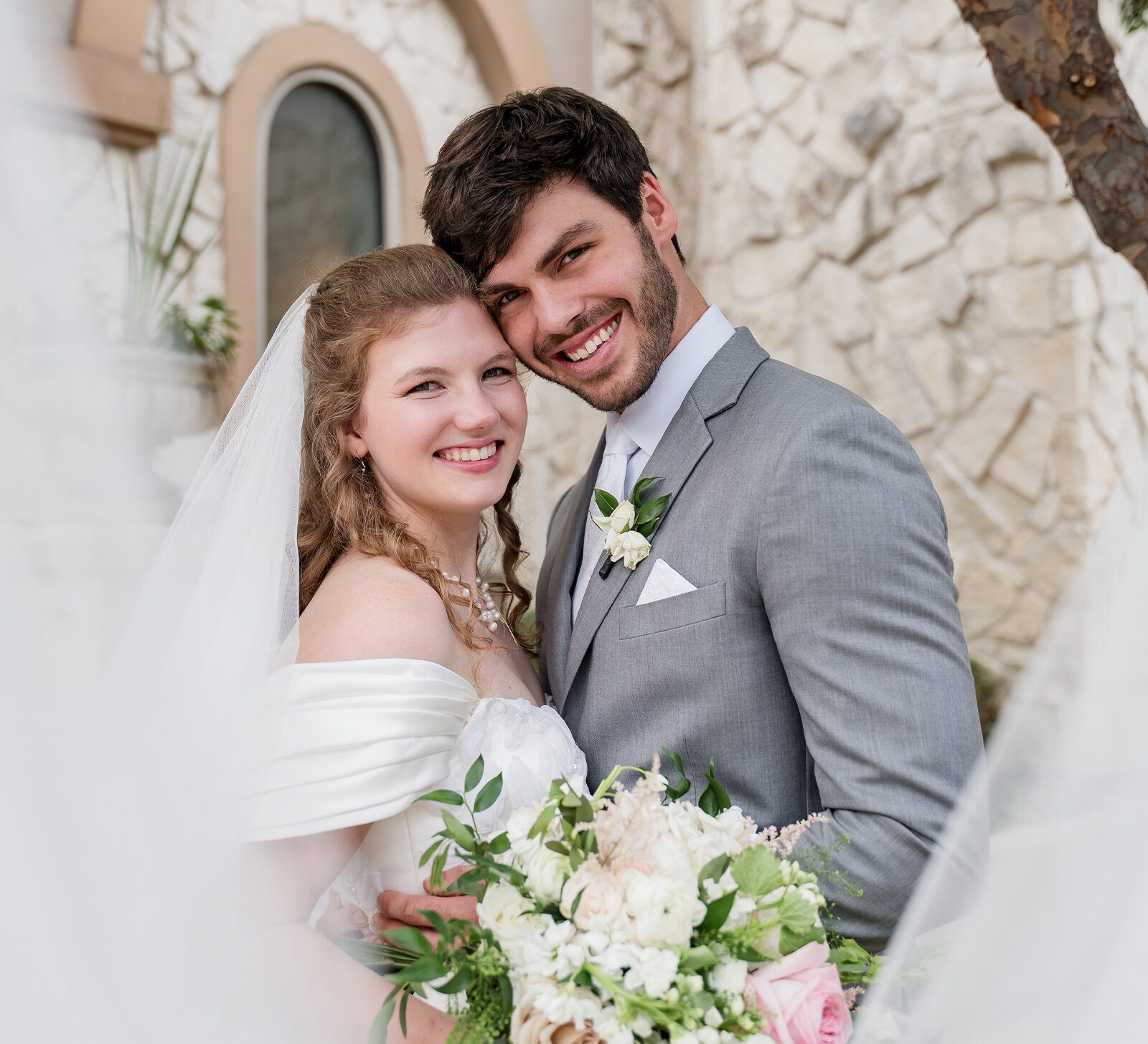 Elegant strapless wedding dress with lace appliqué and tulle skirt hanging on a mirror in a bridal suite.