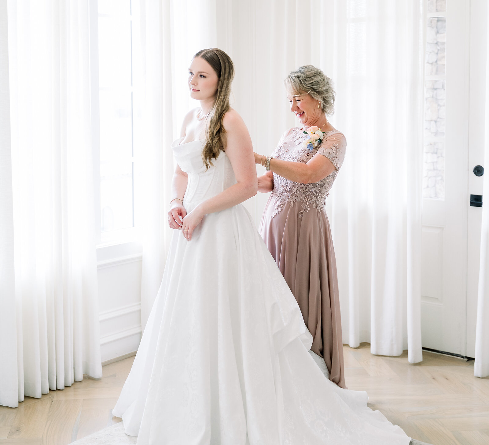 Back view of a bride wearing an elegant strapless wedding gown with sheer lace gloves and a fitted skirt, posing against a textured terracotta wall