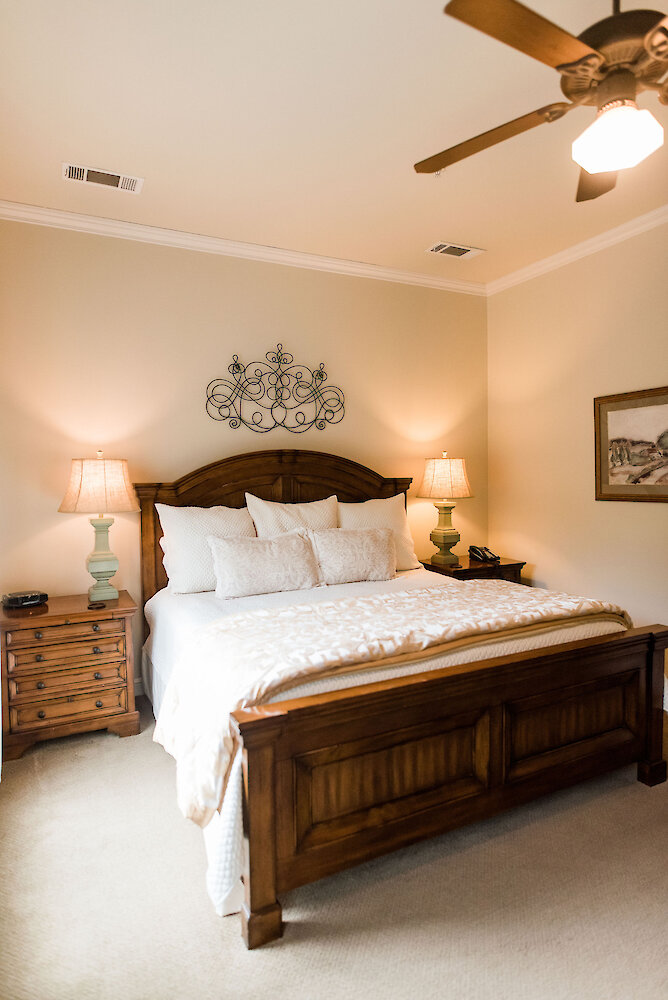 Cozy bedroom with a wooden bed frame, neutral bedding, matching wooden nightstands with lamps, and decorative wall art above the headboard.