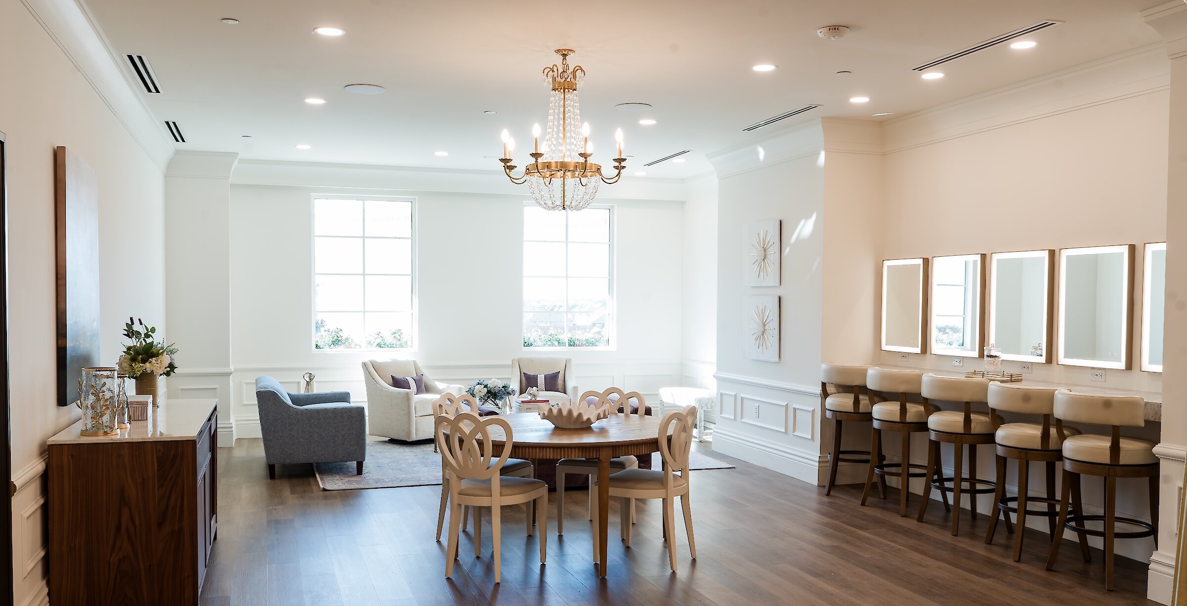 A luxurious and spacious bridal suite featuring a comfortable lounge area, a dining table, and a dedicated makeup station with lighted mirrors.