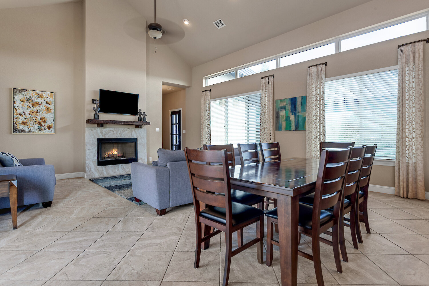Open-concept living and dining room with large windows, wooden dining table, fireplace, and modern decor