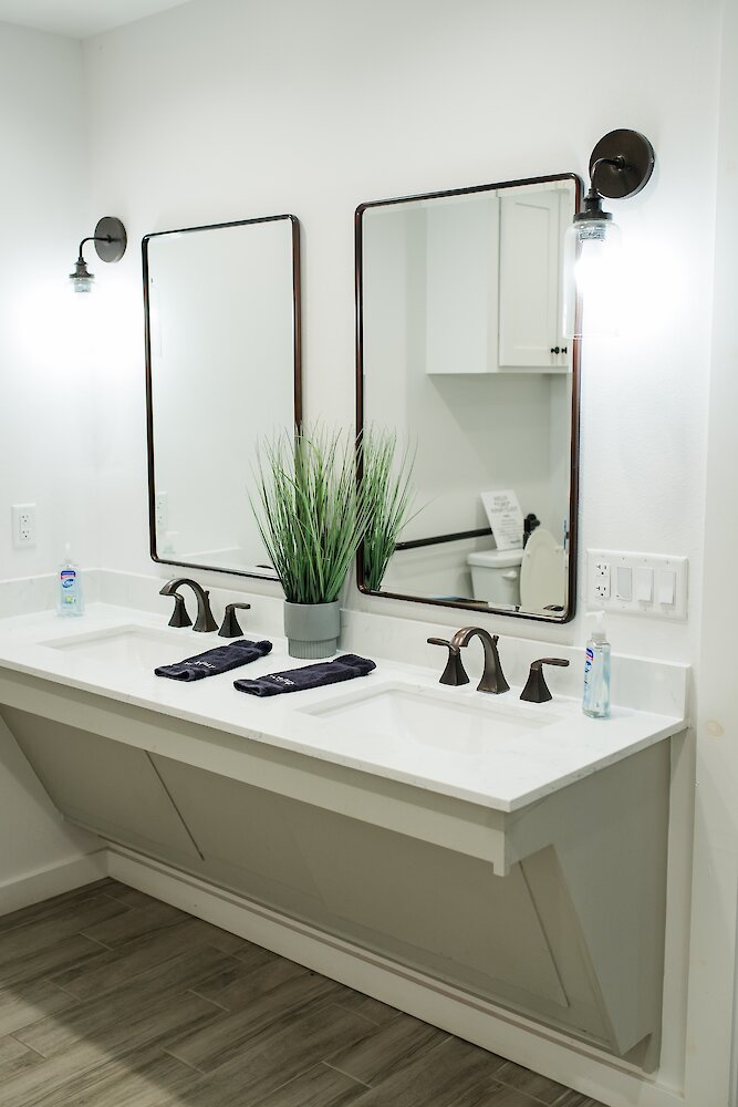 A clean, modern double bathroom vanity with copper faucets, two framed mirrors, and a potted plant in the center.
