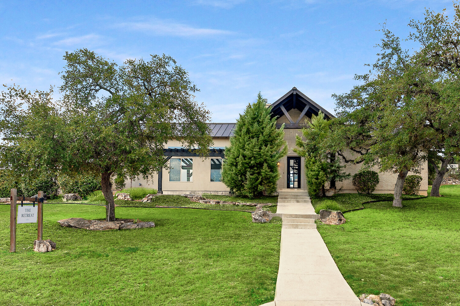 Exterior view of the Retreat building with stone pathway, large trees, and landscaped green lawn under a clear sky.