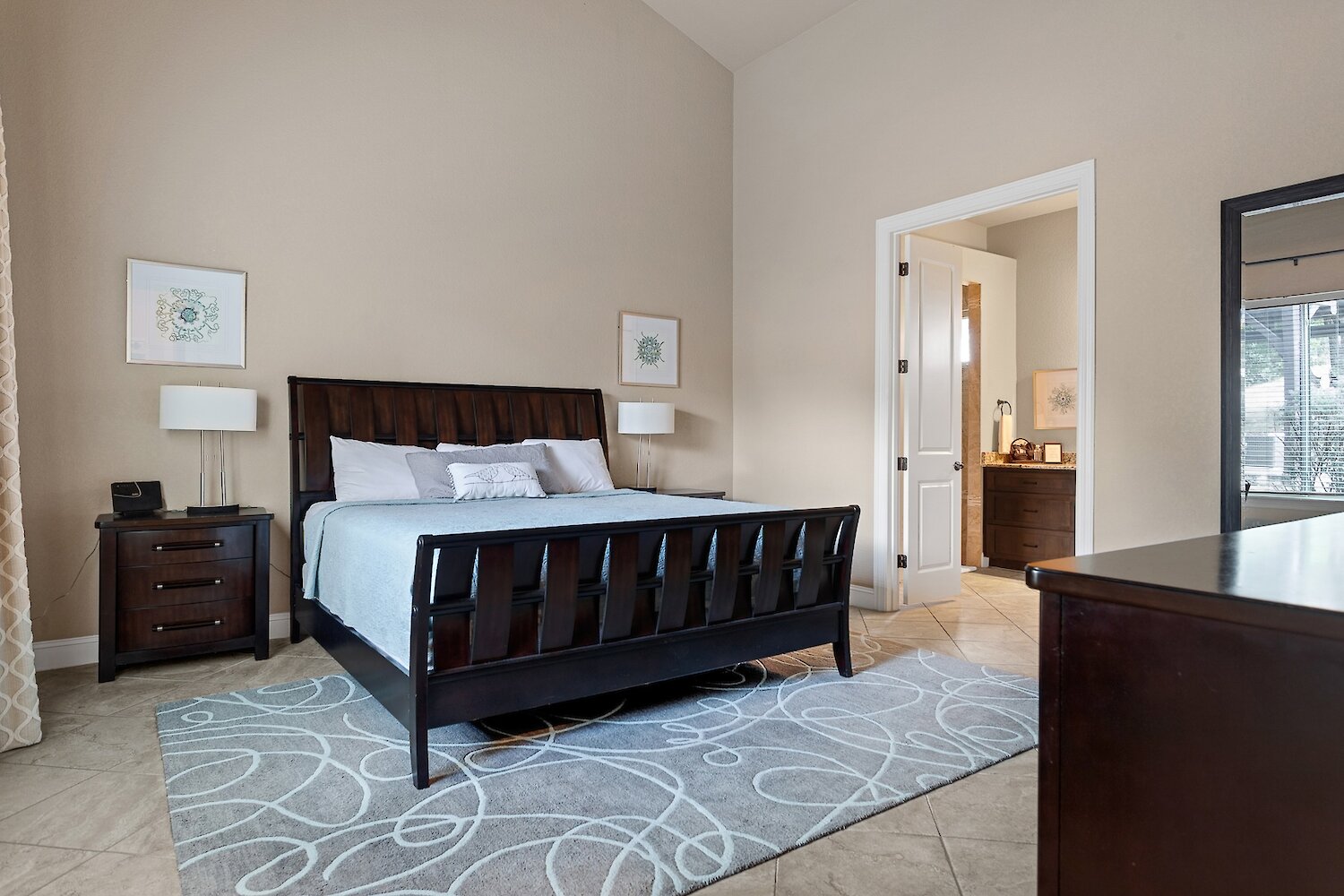 A bright guest bedroom featuring a dark wood sleigh bed with a blue quilt, light beige walls, and a patterned grey and white rug.