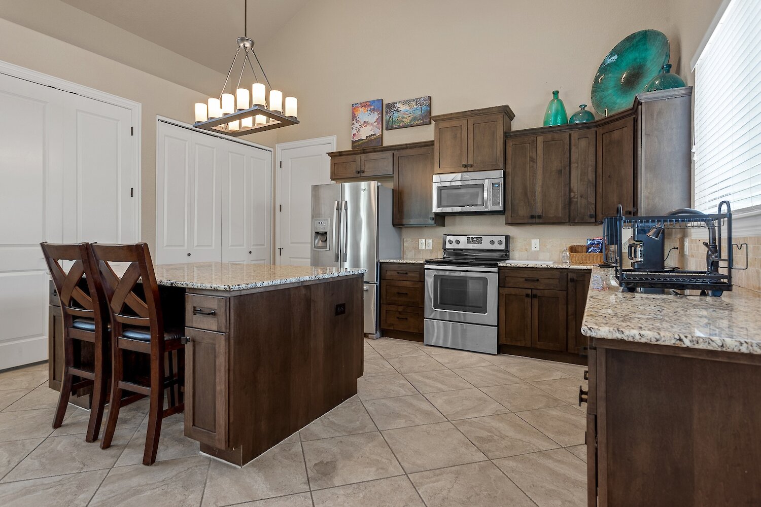 Modern kitchen with dark espresso wood cabinets, stainless steel appliances, and a large central island with granite countertops and bar seating.