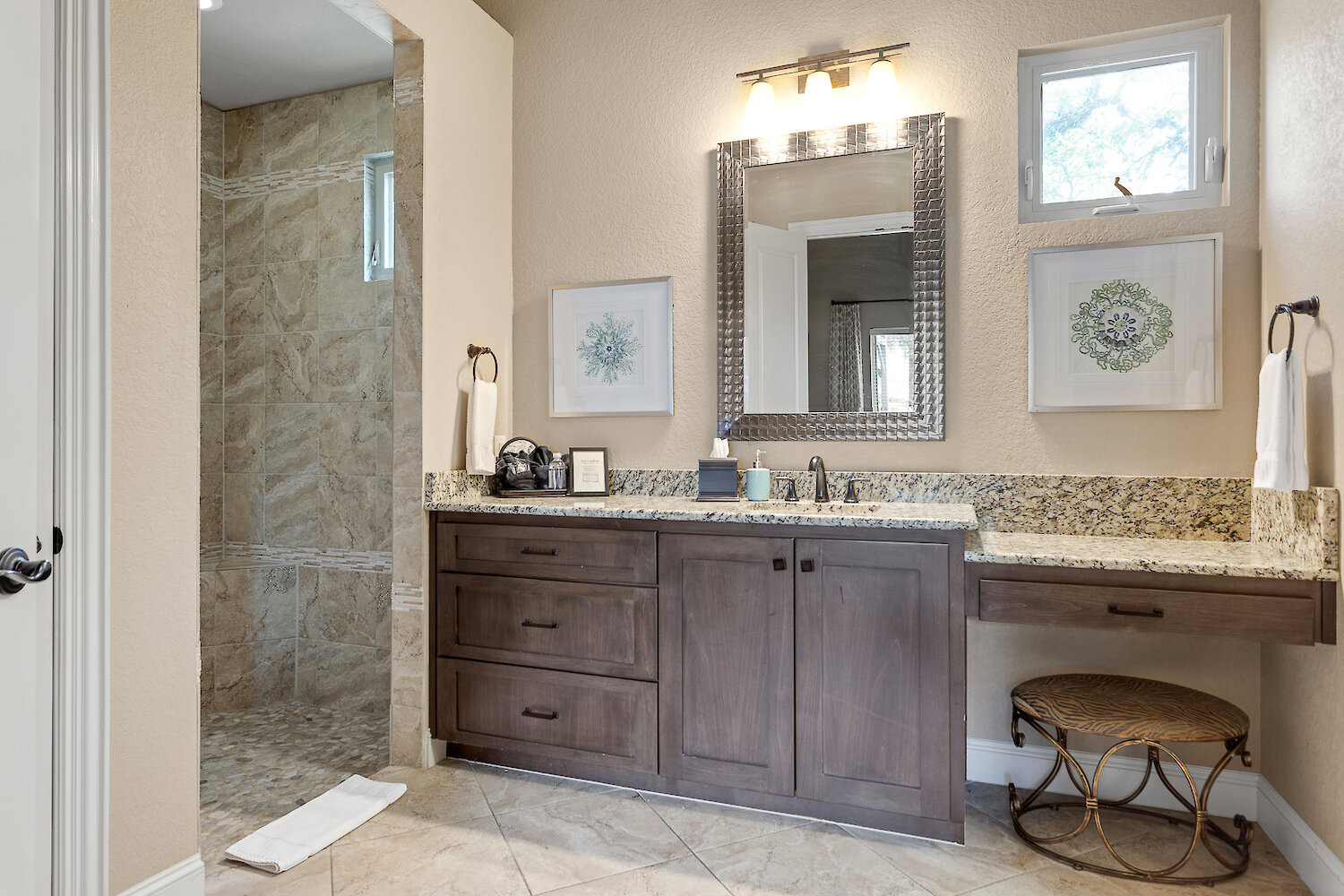 Elegant primary bathroom with dark wood vanity, speckled granite countertop, framed mirror, and a walk-in shower with natural stone tile and a pebble floor.