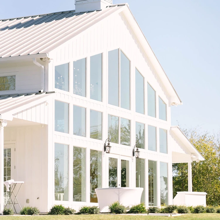 A stunning modern white wedding barn venue featuring a large wall of tall windows and a cupola on the roof.