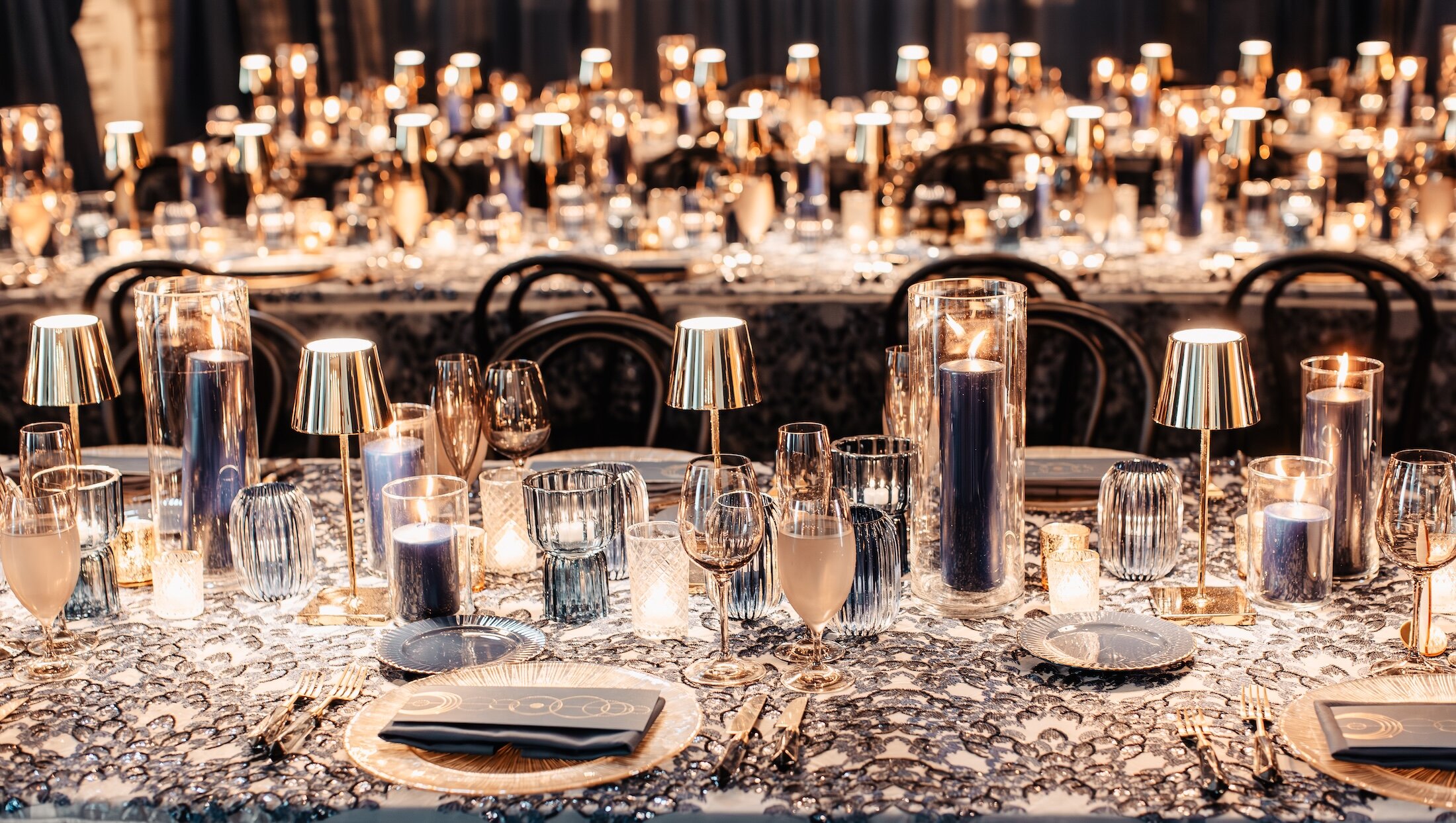 A luxurious wedding reception table set with gold and deep blue accents, numerous candles, and crystal glasses.