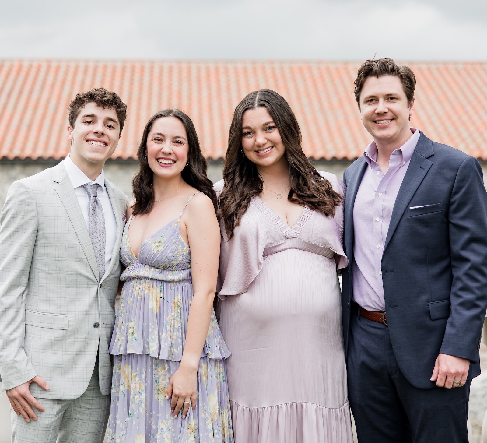 A happy couple and two friends pose for a photo on a stone terrace with a terracotta roof behind them.