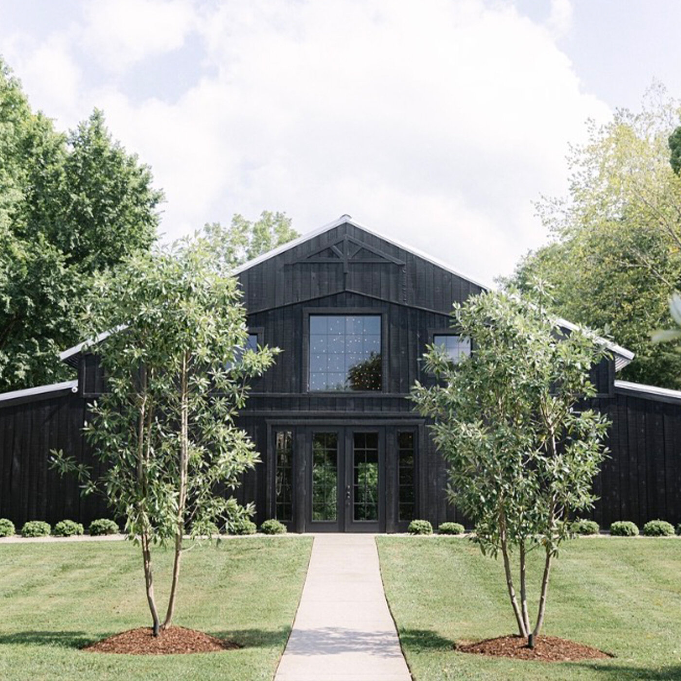 Outdoor wedding ceremony setup featuring a wooden pavilion altar with exposed beams, rows of white folding chairs, a flagstone aisle, and floral arrangements of white and blue hydrangeas, all set beneath large oak trees.