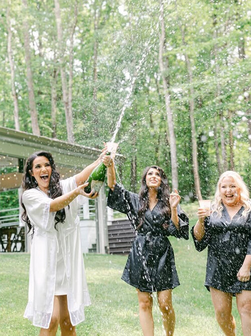 Rustic outdoor wedding portrait featuring the groom dipping and kissing the bride on a grassy lawn in front of a sprawling ranch venue. The bride wears a lace gown and white cowboy boots.