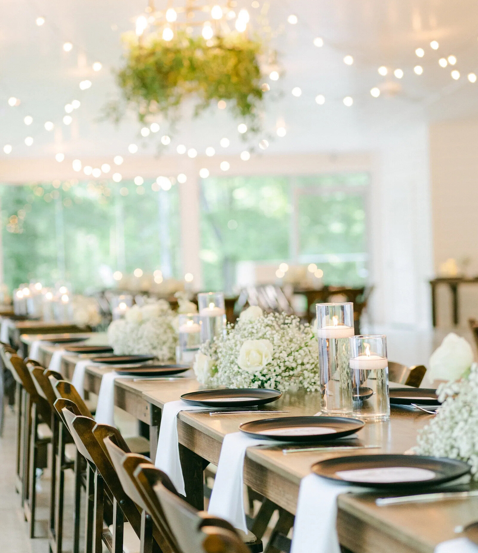 Reception ballroom with tables and string lights with floor to ceiling windows