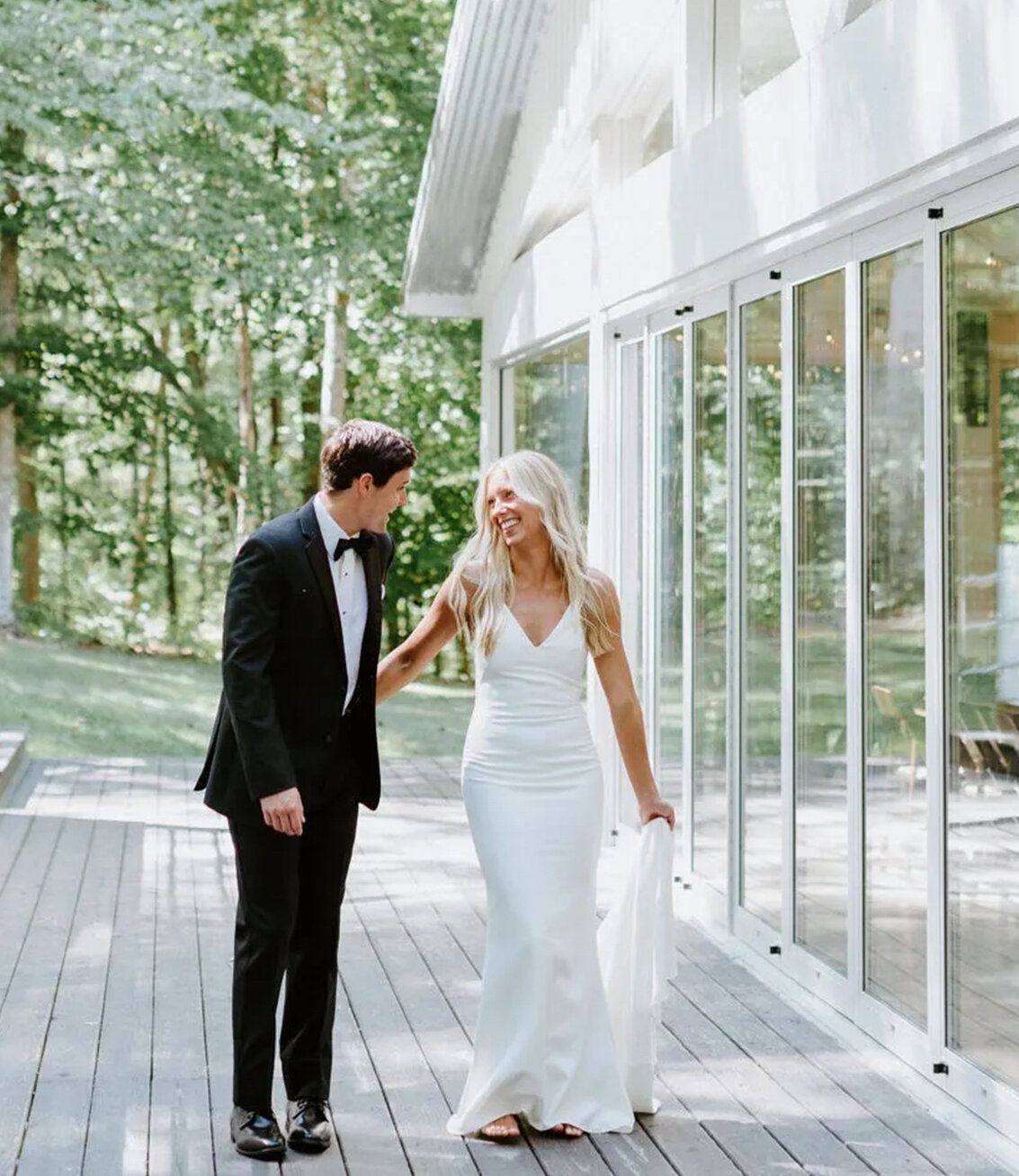 bride and groom holding hands walk outside of glass reception hall