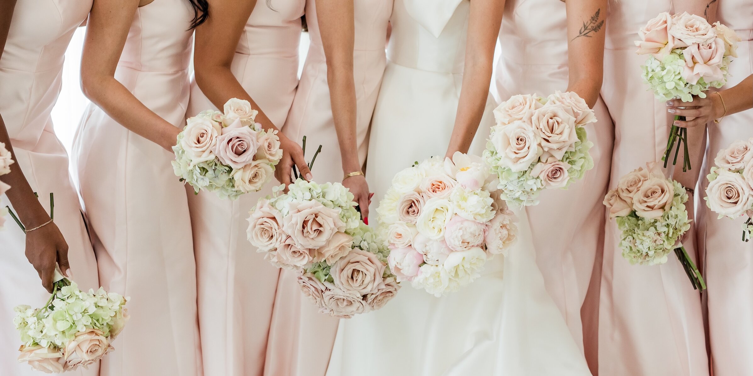Close-up of bridal party holding bouquets so only dresses, arms and hands are seen