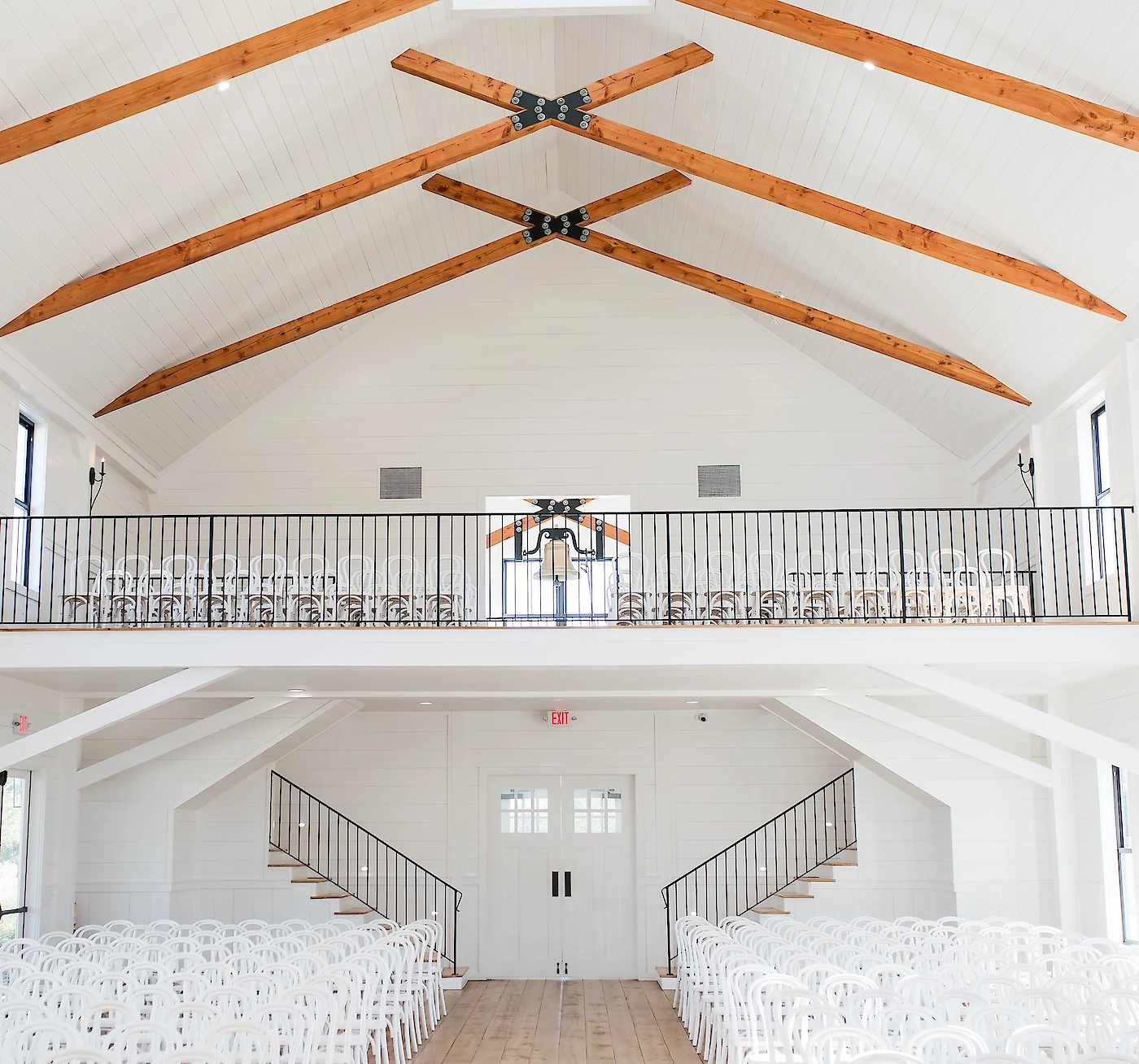 The bright interior of the Arrowhead Hill wedding chapel featuring a vaulted white ceiling with wood beams, a second-floor balcony, and rows of white chairs.