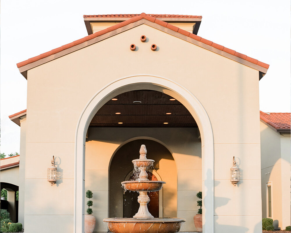 The exterior of a wedding venue featuring a stone facade, clay tile roof, arched windows, and a second-story balcony.