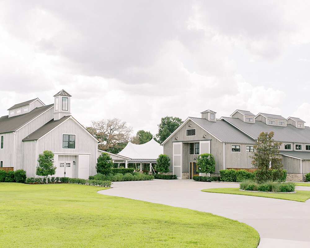 A light-colored limestone chapel features a dark wooden pergola over a patio and is surrounded by lush green landscaping.