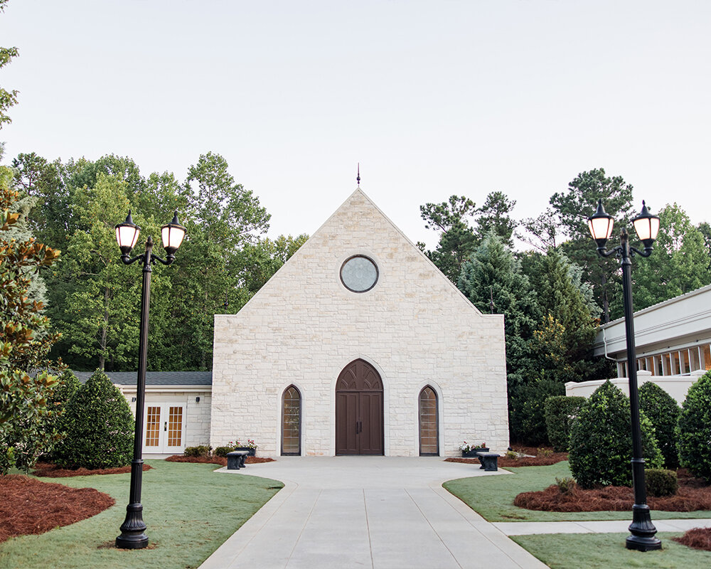 The stone exterior of the Ashton Gardens Atlanta wedding chapel featuring a pointed roof, arched doors, and a round stained glass window.