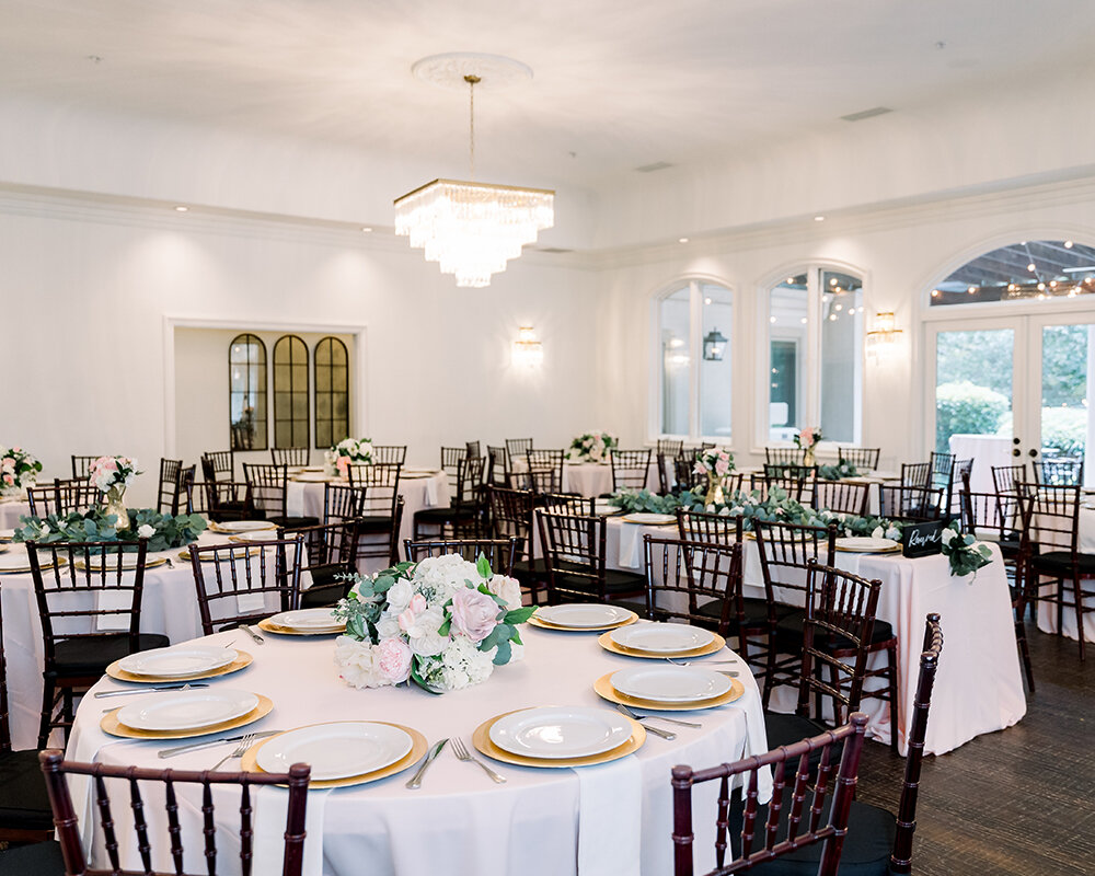 A wedding reception room with round and long tables draped in pink linen, dark wood chiavari chairs, and a chandelier.