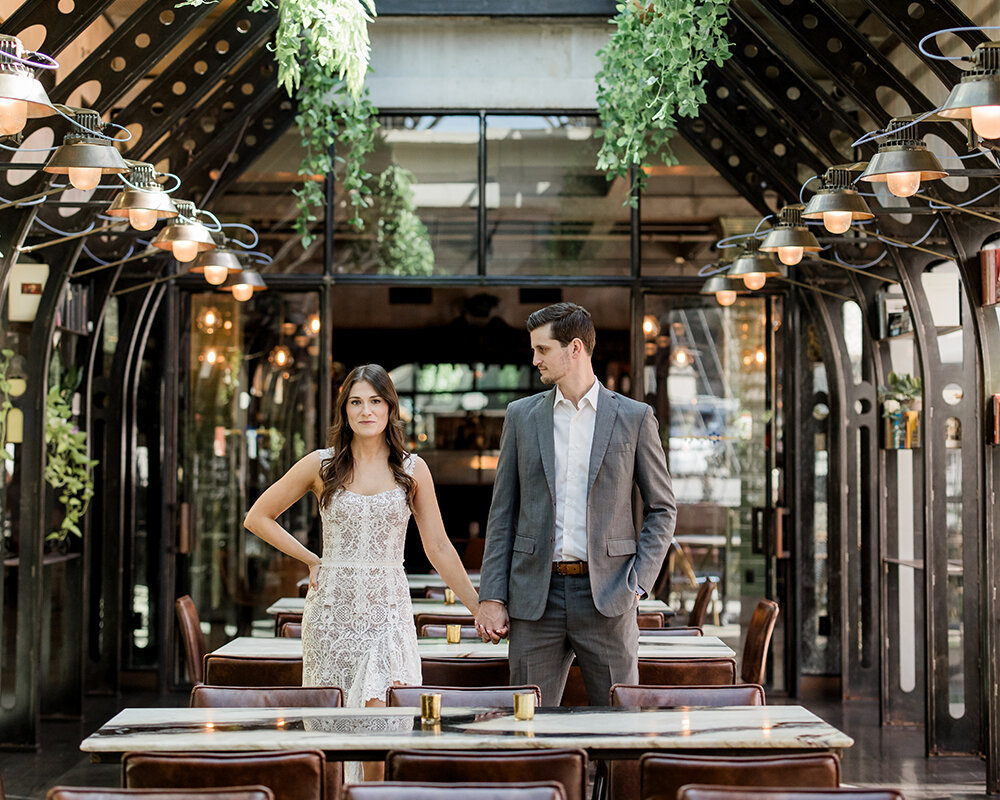 A black and white photo of a happy couple sitting on a leather booth in a dark bar, holding cocktail glasses.