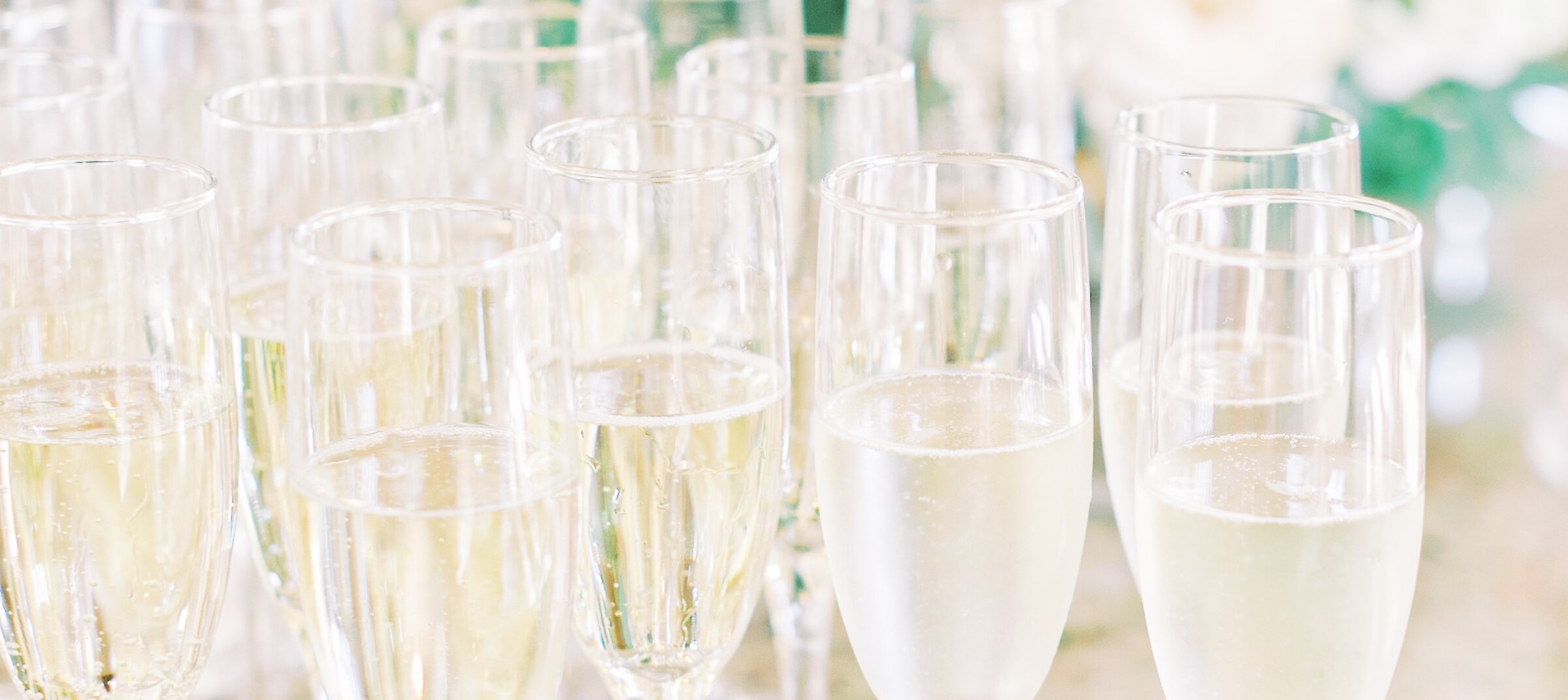 A cluster of champagne flutes filled with bubbly light yellow liquid sit on a mottled marble table during a celebration.