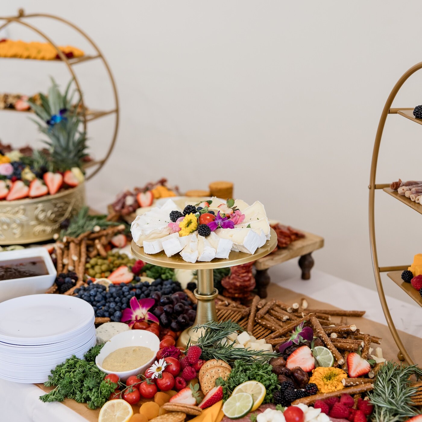 An elaborate wedding charcuterie grazing table featuring cheeses, berries, pretzels, and decorated with colorful edible flowers.