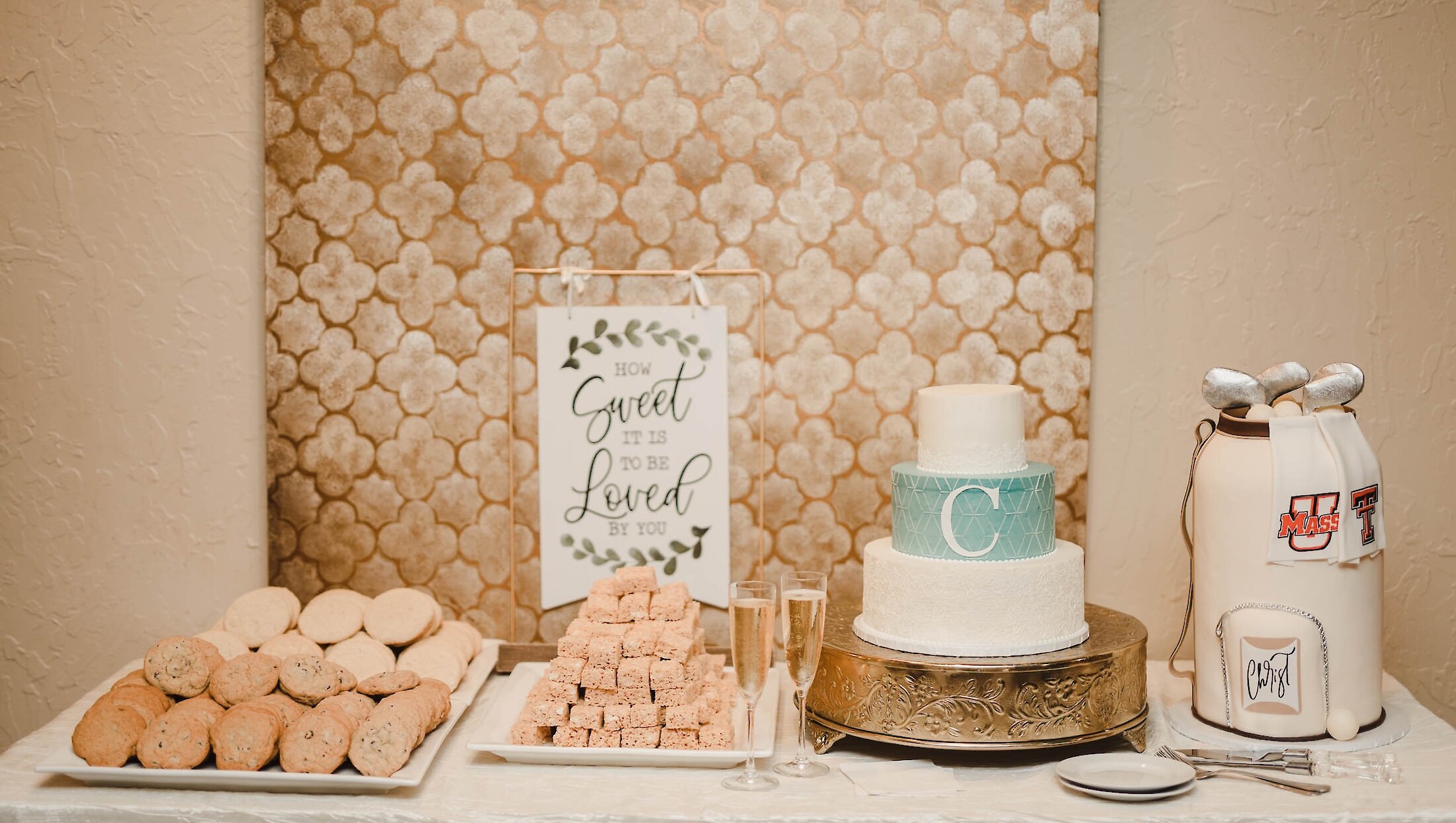 A wedding dessert table featuring a three-tier cake with blue accent, cookies, rice krispie treats, and a groom's cake styled like a golf bag.