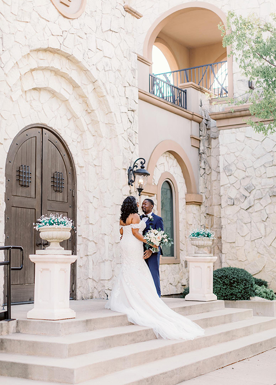 Bride and groom standing on entrance steps in front of tan stone Tuscan venue