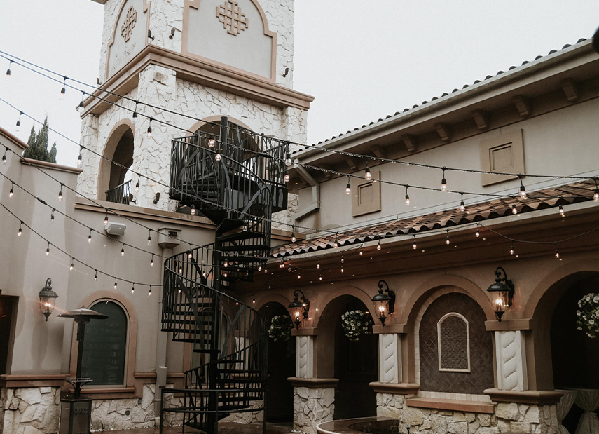 Angled view of Tuscan-inspired courtyard with spiral staircase and bistro lights